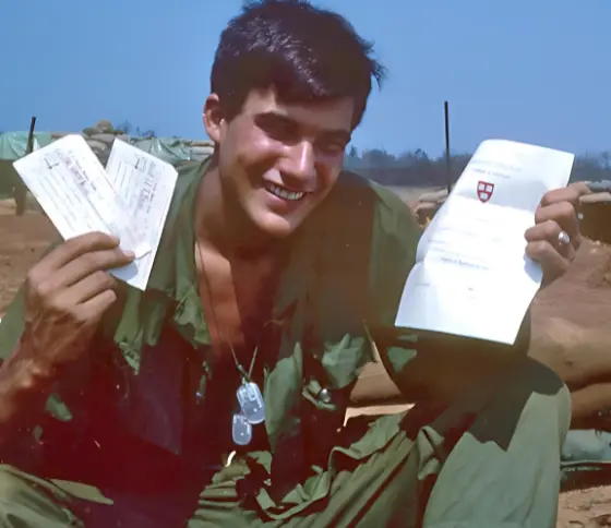 Jack McLean in Vietnam holding up Harvard acceptance letter and two plane tickets home